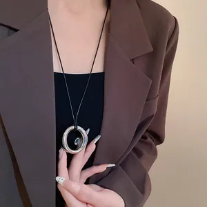 Gros plan d'un pendentif rond argenté minimaliste sur un cordon en cuir noir porté en détail.