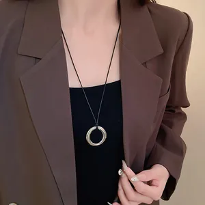 Vue détaillée d'un collier pendentif rond en argent avec cordon noir porté sur un blazer marron.