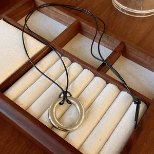 Gros plan d'un pendentif circulaire argenté minimaliste sur un long cordon noir