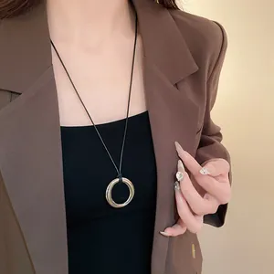 Gros plan d'un collier minimaliste avec pendentif circulaire argenté et cordon cuir.