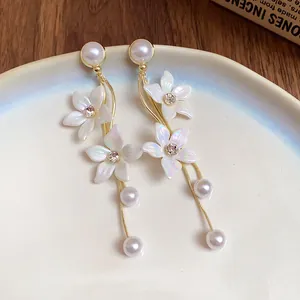 Detail von eleganten Ohrringen mit schillernden Blumen und Perlen an feinen Goldketten