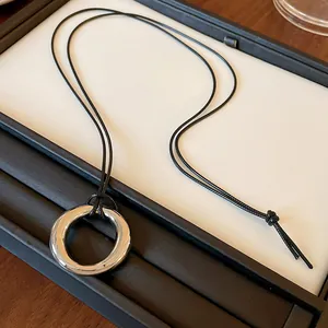 Vue détaillée d'un pendentif circulaire argenté minimaliste sur un cordon noir