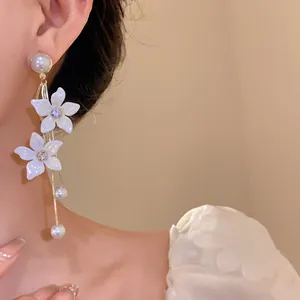 Detailaufnahme eleganter weißer Blumenohrringe mit Perlenquasten und Kristallmitten