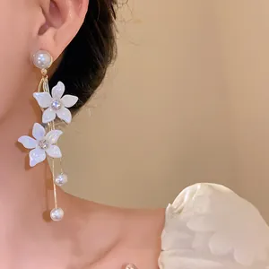 Detailansicht eleganter weißer Blumenohrringe mit hängenden Perlenquasten und Kristallen.