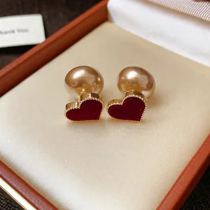 Close-up detail of elegant red velvet heart earrings with gold beaded edges and pearl back.