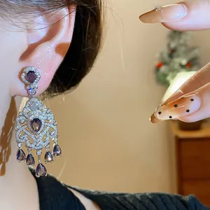 Close-up of vintage palace style teardrop earrings with purple zircons worn on ear.