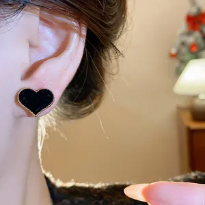 Close-up showing the soft flocked texture of a black heart stud earring on a female ear