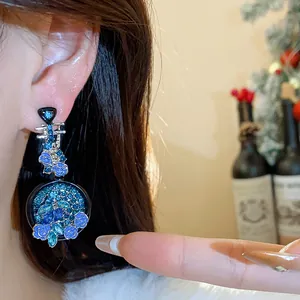 Elegant pipa-shaped earrings featuring blue floral patterns and shimmering crystals worn on ear