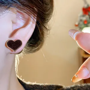 Close-up detail showing the texture of a dark flocked heart stud earring worn on an ear