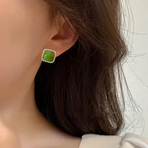 Close-up of a minimalist green square stud earring with a silver beaded frame worn on an ear.