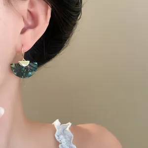 Close-up view of a retro fan-shaped drop earring with green marbled texture on model