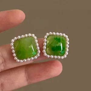Close-up of green square stud earrings with marbled pattern and faux pearl border