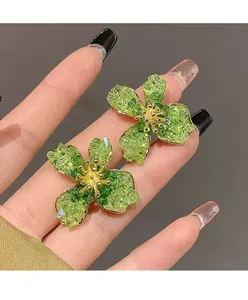 Macro close-up of green flower stud earrings with silver needles and gold center detail