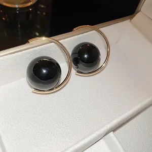 Detailed view of gold-plated hoop earrings with large black pearls in a gift box
