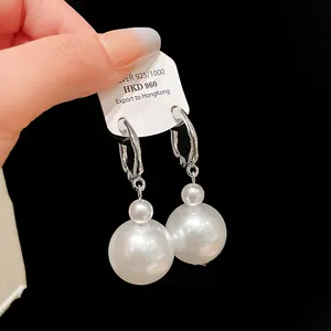 Detail of elegant pearl drop earrings featuring glossy white pearls and silver hoops.