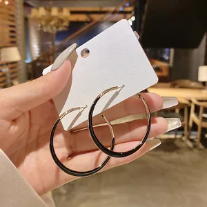 Person holding elegant large gold hoop earrings with black enamel finish on a white card