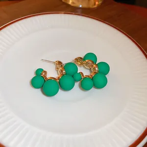 Macro view of matte green bead flower earrings with gold finish on a white plate