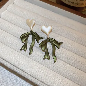 Close-up of green bow earrings with white pearlescent heart studs in a display tray.