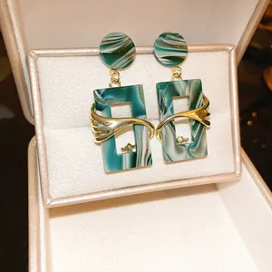 Detailed view of green marble geometric earrings with gold wave accents in a gift box