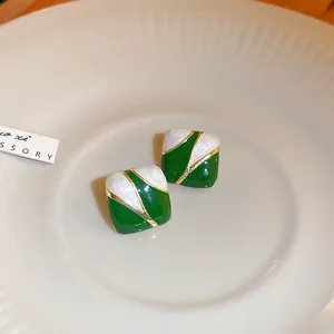 Close-up of vintage-style green and white square stud earrings on a ceramic plate