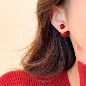 Dettaglio ravvicinato di orecchini a perno con doppie perle rosse su una modella