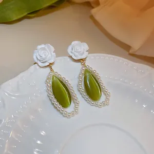 Macro detail view of green cat-eye teardrop earrings with white rose and pearl accents