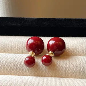 Dettaglio di eleganti orecchini a doppia perla rosso scuro lucido con finitura dorata