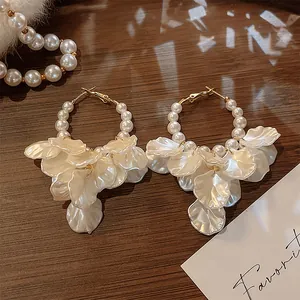 Detailed view of elegant vintage shell petal hoop earrings with pearls on wood tray