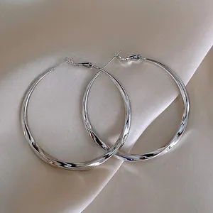 Elegant silver twisted hoop earrings on beige silk background, large minimalist design