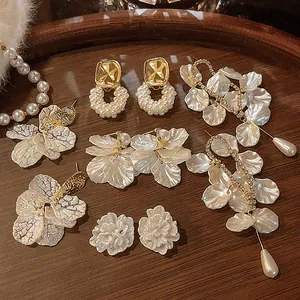 Detailed view of vintage French shell petal and pearl tassel earrings on a wooden tray