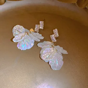 Close-up of iridescent shell petal earrings with clear crystal geometric accents