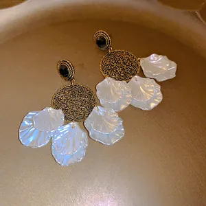 Macro detail of French vintage earrings with white shell petals and gold filigree.
