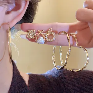 Detailansicht von goldenen Ohrringen im Set mit Creolen, Perlen und Kristallsteckern.