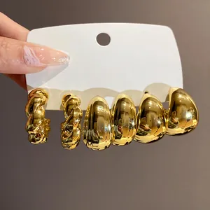 Nahaufnahme eines goldenen geometrischen Tropfen- und Creolen-Ohrring-Sets.