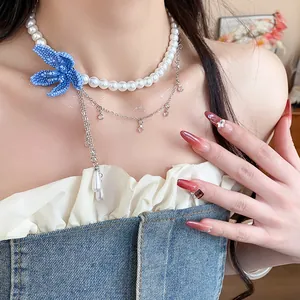 Detailed close-up of a pearl necklace featuring a blue beaded flower and teardrop pendant.