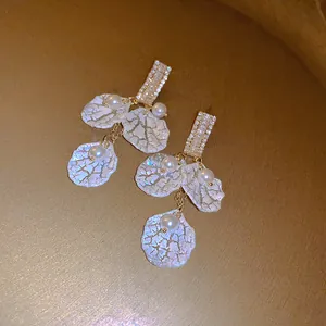 Close-up of elegant French vintage shell petal drop earrings featuring pavé crystals and pearls