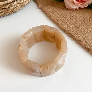 Close-up detail of a marbled acrylic rectangular block elastic bracelet in a beige tone