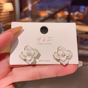Gros plan de boucles d'oreilles clous élégantes en forme de camélia blanc sur carte.