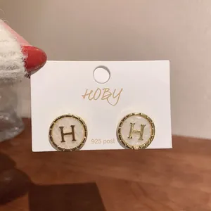 Détail de boucles d'oreilles dorées circulaires lettre H avec tiges en argent 925.