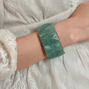 Close-up of a green marbled acrylic rectangular stretch bracelet worn on a woman's wrist