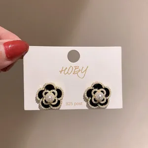 Vue détaillée d'élégantes boucles d'oreilles camélia noires avec perles et accents dorés.