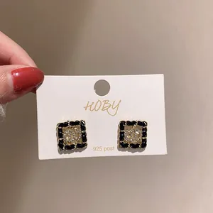 Détail de boucles d'oreilles vintage carrées avec bordure noire et logo cristal