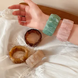 Detailed view of colorful rectangular marble-patterned acrylic elastic bracelets on white fabric