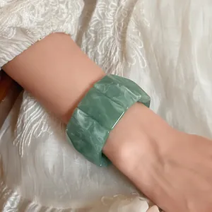 Close-up of green marble acrylic elastic bracelet worn on wrist with white lace outfit.