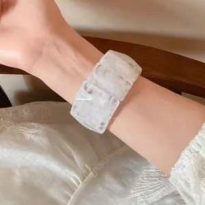 Close-up view of a rectangular acrylic marble bracelet on a wrist with white lace sleeve.
