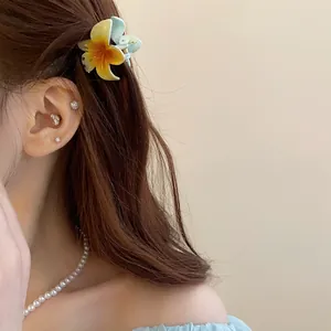 Vue détaillée d'une mini pince à cheveux fleur de frangipanier sur des cheveux bruns