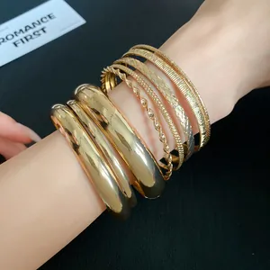 Stack of gold-toned textured bangles on model's wrist with various geometric patterns