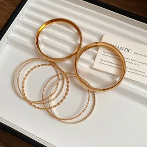 Stack of gold geometric metal bangles with twisted and textured patterns on a white tray