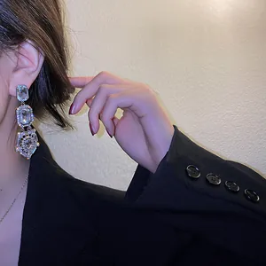 Elegant sparkling geometric crystal drop earrings worn by a model in a black blazer