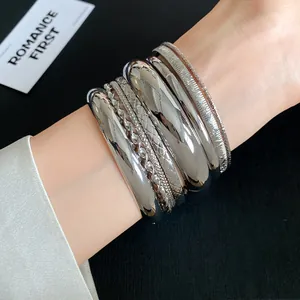 Detailed view of a 7-piece silver metallic geometric textured bangle set on a wrist.